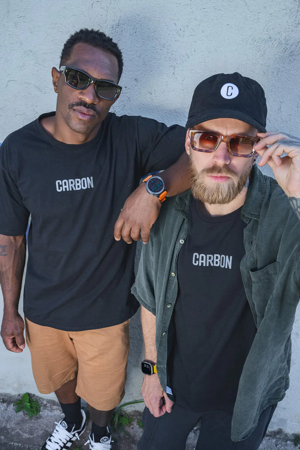 Dois homens com camiseta CARBON e relógio Carbon no pulso, encostados num muro